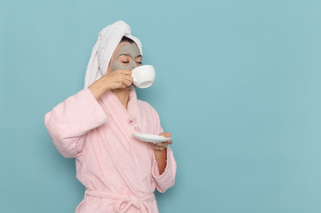 Vooraanzicht jonge vrouw in roze badjas koffie drinken op blauwe muur schoonmaken schoonheid schoon water zelfzorg crème douche