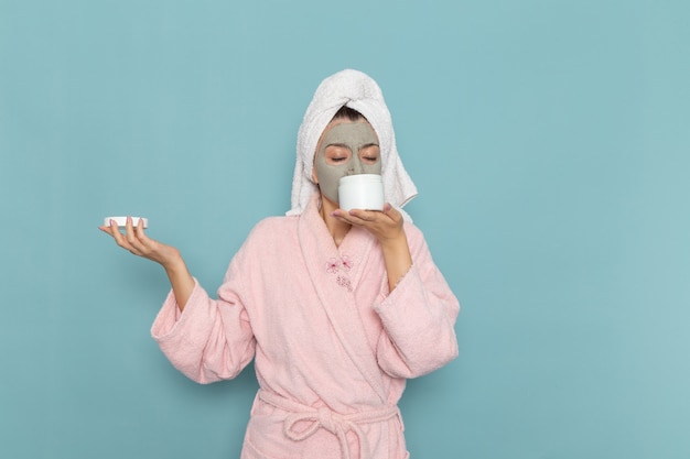 Vooraanzicht jonge vrouw in roze badjas met crème op de blauwe muur schoonheid water bad crème zelfzorg douche