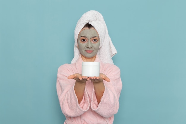 Vooraanzicht jonge vrouw in roze badjas met masker op haar gezicht met crème kan op de blauwe muur douche schoonmaken schoonheid zelfzorg crème