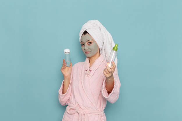 Vooraanzicht jonge vrouw in roze badjas na douche met sprays op de blauwe muur schoonheid water crème zelfzorg douche