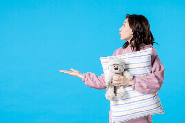 Vooraanzicht jonge vrouw in roze pyjama met kleine speelgoedbeer en kussen op blauw slapeloosheid bed nacht nachtmerrie droom feest rust slaap