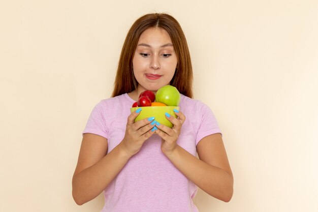 Vooraanzicht jonge vrouw in roze t-shirt en spijkerbroek met plaat met fruit