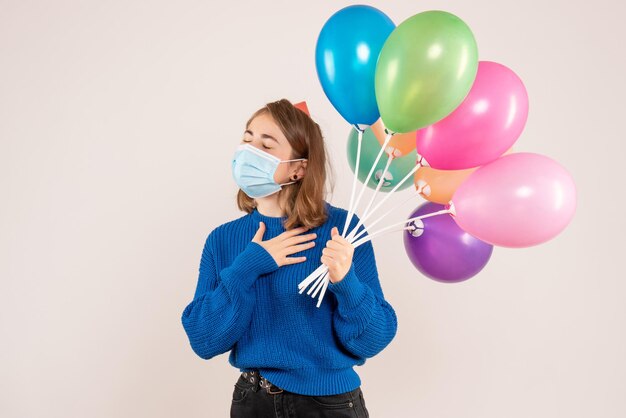 Vooraanzicht jonge vrouw in steriel masker met kleurrijke ballonnen