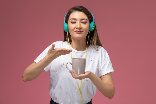 Vooraanzicht jonge vrouw in wit overhemd luisteren naar muziek ruikende koffie op de roze muur, kleur vrouw model vrouw