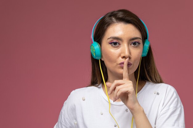 Vooraanzicht jonge vrouw in wit overhemd luisteren naar muziek stilte teken tonen op roze, vrouw model poseren meisje