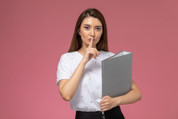 Vooraanzicht jonge vrouw in wit overhemd met stilte teken op de roze muur