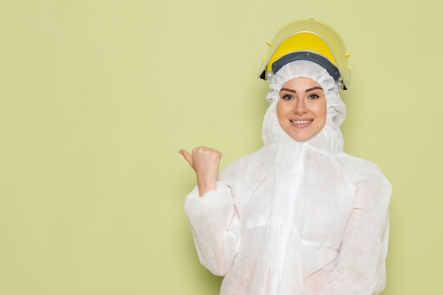 Vooraanzicht jonge vrouw in wit speciaal pak en gele helm glimlachend en poseren op de groene ruimtepak uniforme wetenschap