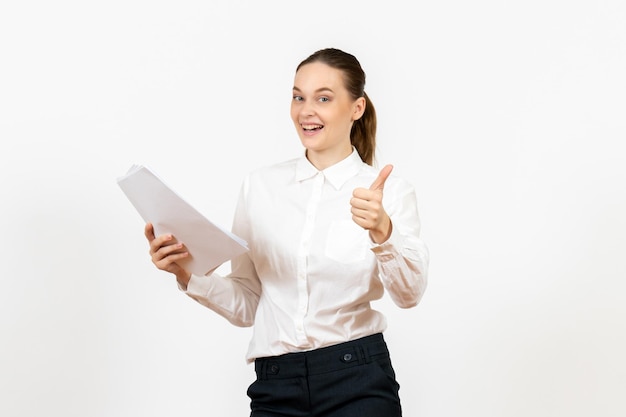 Vooraanzicht jonge vrouw in witte blouse die documenten vasthoudt en glimlacht op een witte achtergrond vrouwelijke baanemoties die kantoor voelen