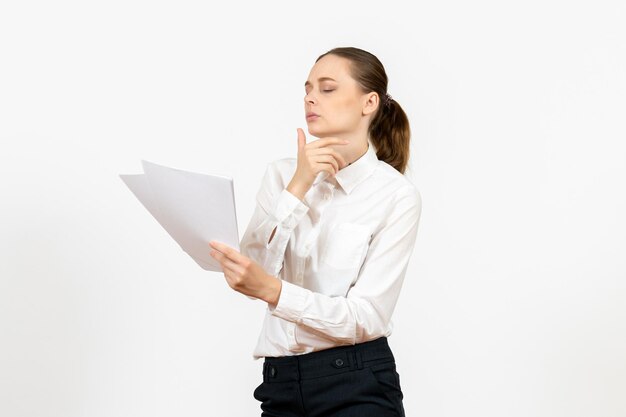 Vooraanzicht jonge vrouw in witte blouse die documenten vasthoudt en leest op een witte achtergrond vrouwelijke baanemotie die kantoor voelt