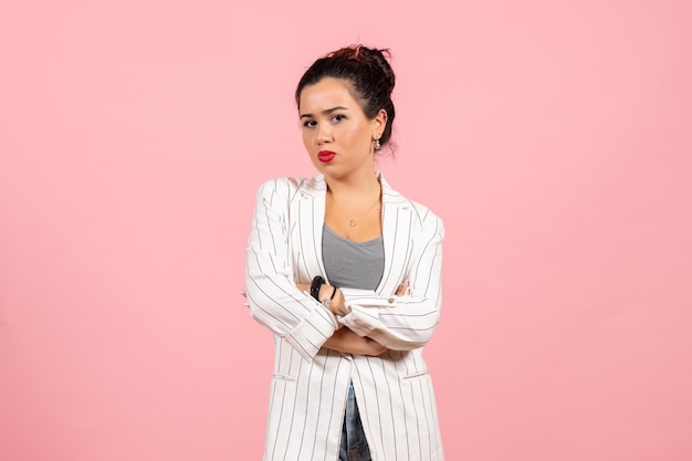 Vooraanzicht jonge vrouw in witte jas poseren op licht roze achtergrond dame mode kleur vrouw emotie fashion