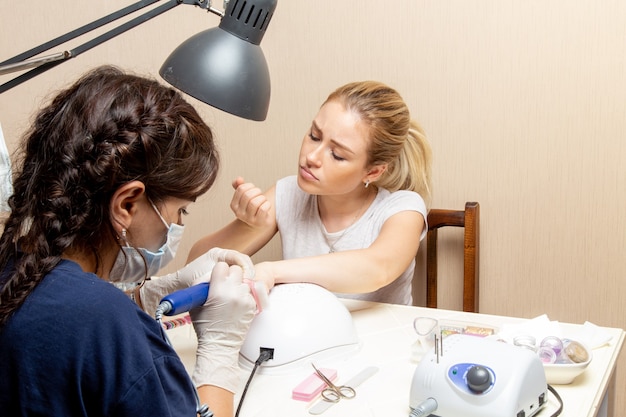 Vooraanzicht jonge vrouw krijgt haar nagels gefixeerd door manicure in kamer schoonheid vrouw manicure nagel zelfzorg dame