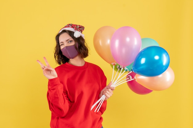 Vooraanzicht jonge vrouw met ballonnen in masker op geel bureau virus covid partij emotie nieuwjaar kleur vrouw