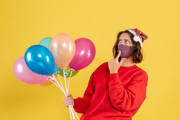 Vooraanzicht jonge vrouw met ballonnen in masker op geel