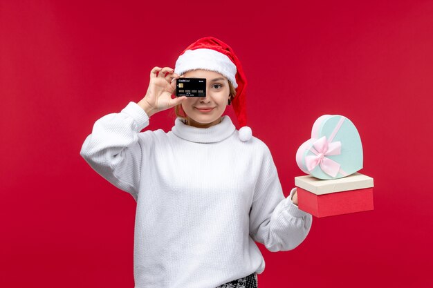 Vooraanzicht jonge vrouw met bankkaart en geschenken op rode achtergrond