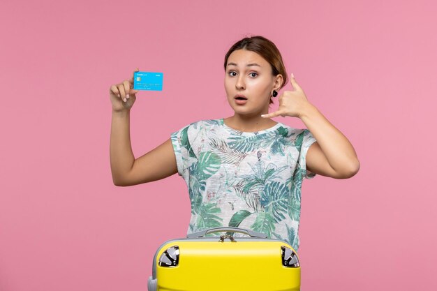 Vooraanzicht jonge vrouw met bankkaart met gele vakantietas op roze bureau rust vlucht reis vliegtuig vrouw