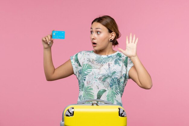 Vooraanzicht jonge vrouw met bankkaart met gele vakantietas op roze bureau vakantie rust vlucht reis vliegtuig vrouw