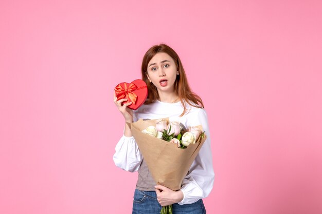 Vooraanzicht jonge vrouw met bloemen en heden als de daggift van de vrouw op roze achtergrond horizontale maart gelijkheid vrouwelijke datum roze vrouw liefde