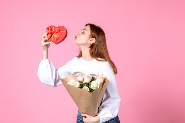 Vooraanzicht jonge vrouw met bloemen en heden als de daggift van de vrouw op roze achtergrond horizontale maart vrouw gelijkheid liefde vrouwelijke datum roos