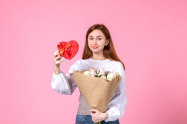 Vooraanzicht jonge vrouw met bloemen en heden als vrouwendag cadeau op roze achtergrond horizontale maart vrouw gelijkheid sensuele vrouwelijke datum roos