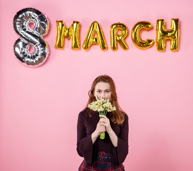 Vooraanzicht jonge vrouw met bloemen in haar handen en maart decoratie op roze achtergrond partij womens dag maart huwelijk passie gelijkheid aanwezig