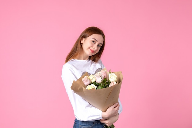 Vooraanzicht jonge vrouw met boeket van mooie rozen op roze