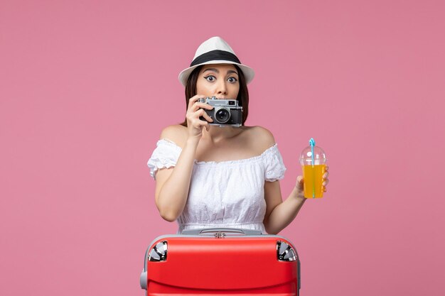 Vooraanzicht jonge vrouw met camera en cocktail op de roze muur kleur vakantie reis warmte zomer reis