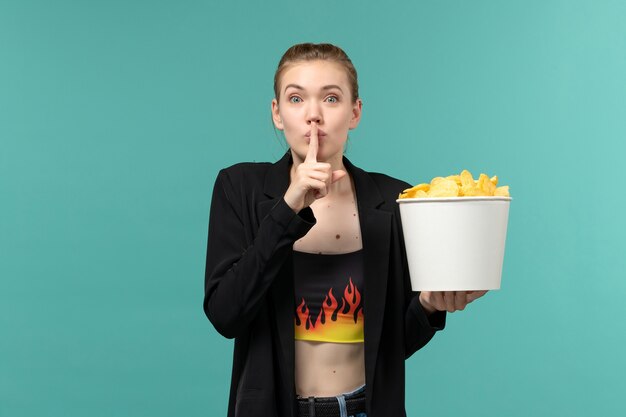 Vooraanzicht jonge vrouw met chips en film kijken op het lichtblauwe oppervlak