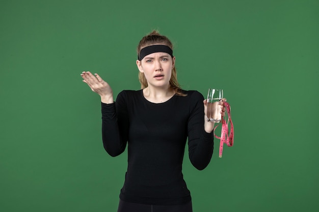 Vooraanzicht jonge vrouw met glas water en taille maatregel op groene achtergrond gezondheid sport lichaam zwarte training vrouw atleet
