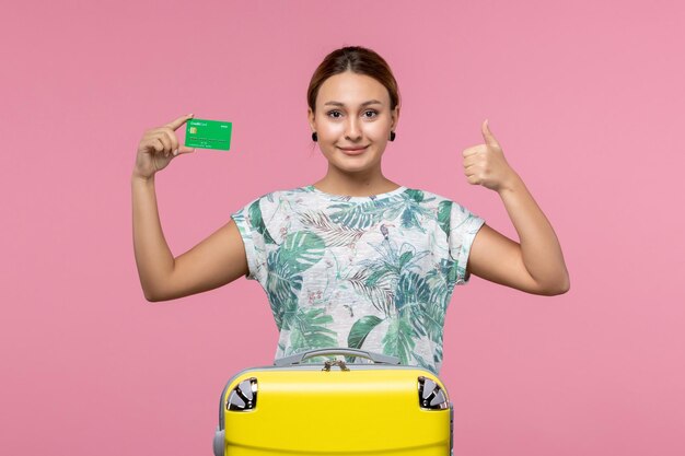 Vooraanzicht jonge vrouw met groene bankkaart op vakantie op de lichtroze muurreis vrouw rust reis zomer