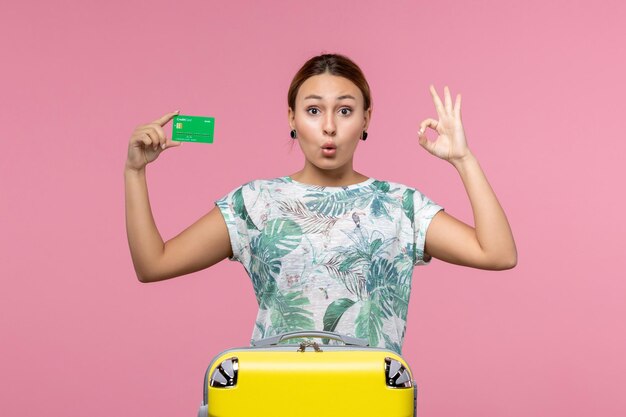 Vooraanzicht jonge vrouw met groene bankkaart op vakantie op de roze muur reis vrouw reis zomer rust