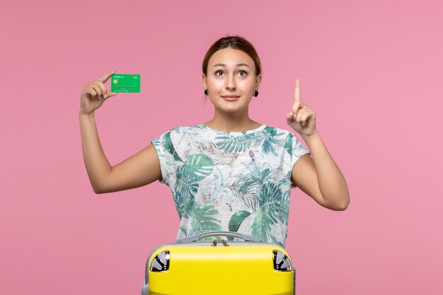 Vooraanzicht jonge vrouw met groene bankkaart op vakantie op de roze muur reis vrouw rust reis zomer