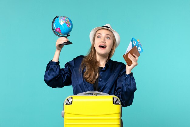 Vooraanzicht jonge vrouw met kaartjes en kleine wereldbol op blauwe achtergrond vliegtuig vakantie reis reis zee