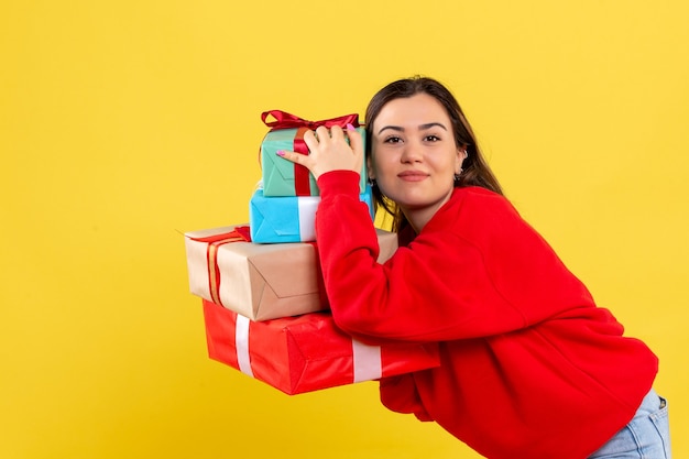 Vooraanzicht jonge vrouw met kerstcadeaus op gele achtergrond
