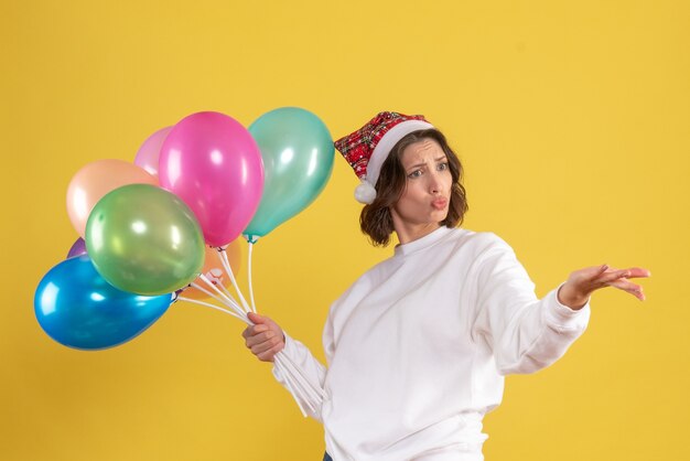 Gratis foto vooraanzicht jonge vrouw met kleurrijke ballonnen op geel