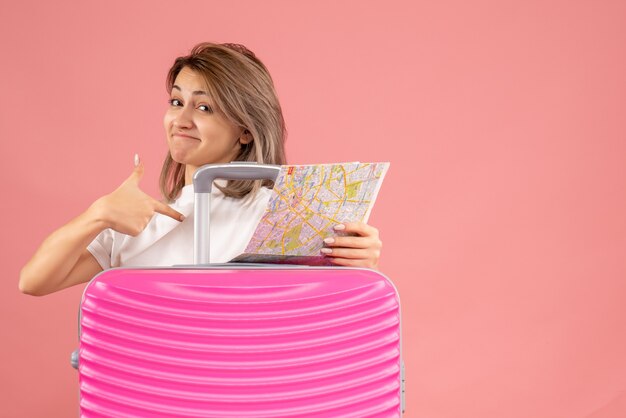 Vooraanzicht jonge vrouw met roze koffer met kaart die naar zichzelf wijst