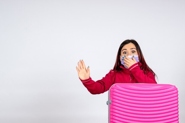 Vooraanzicht jonge vrouw met roze zak in masker op witte muur virus vrouw vakantie covid kleur pandemie reis