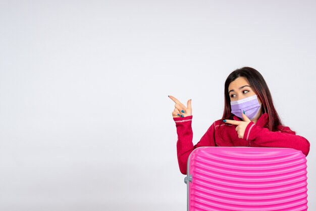Vooraanzicht jonge vrouw met roze zak in steriel masker op witte muur reis kleur vakantie covid-vrouw pandemie