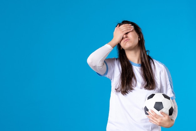 Vooraanzicht jonge vrouw met voetbal op blauwe muur