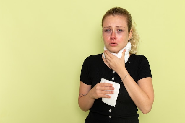 Gratis foto vooraanzicht jonge vrouw met witte handdoek om haar keel erg ziek en ziek voelen op de groene muur ziekte ziekte vrouwelijke kleur gezondheid