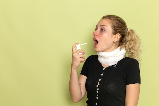 Vooraanzicht jonge vrouw met witte handdoek om haar keel zich erg ziek en ziek voelen met behulp van spray op groene muur ziekte ziekte vrouwelijke gezondheid