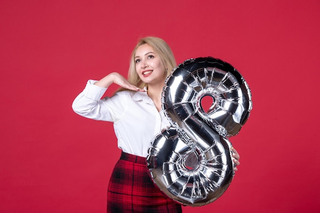 Vooraanzicht jonge vrouw met zilveren ballon als maart-symbool op rood