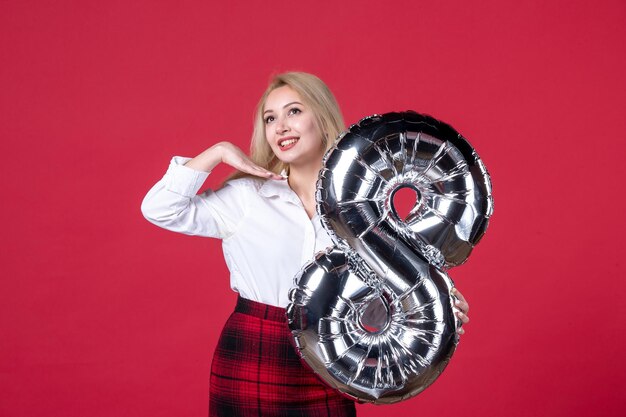 Vooraanzicht jonge vrouw met zilveren ballon als maart-symbool op rood