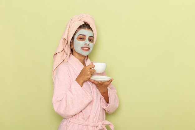 Vooraanzicht jonge vrouw na douche in roze badjas koffie drinken op groene ondergrond