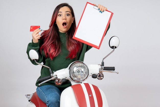 Vooraanzicht jonge vrouw op motorfiets met notitie en bankkaart op witte muur