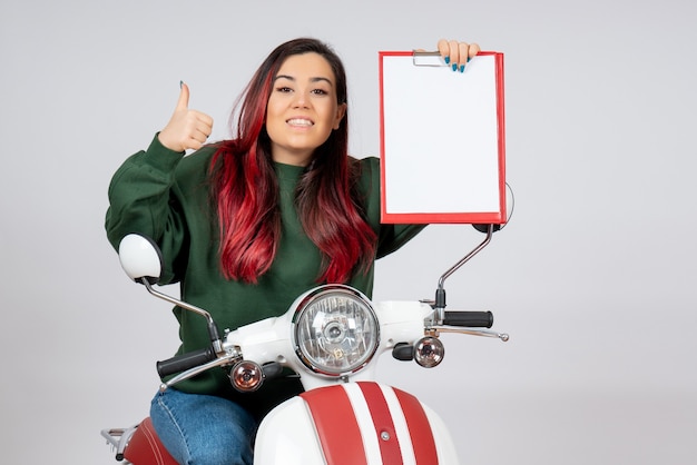Vooraanzicht jonge vrouw op motorfiets met notitie voor handtekening op witte muur