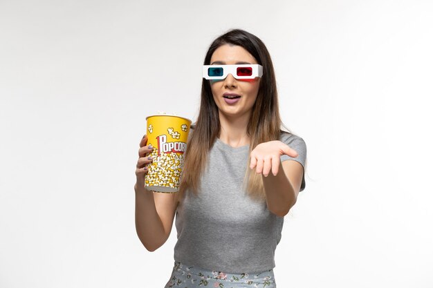 Vooraanzicht jonge vrouw popcorn eten en kijken naar film in d zonnebril op witte ondergrond