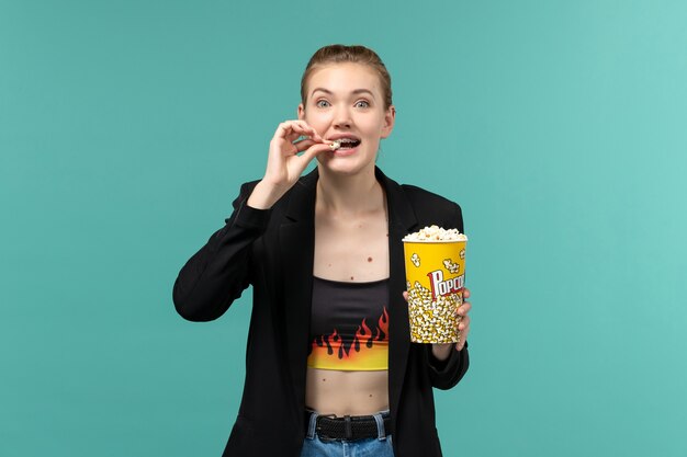 Vooraanzicht jonge vrouw popcorn eten en kijken naar film op het blauwe oppervlak