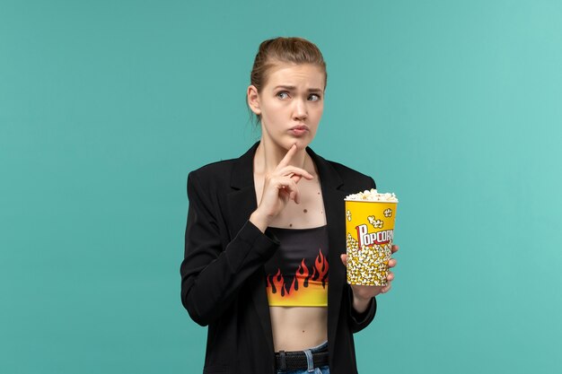 Vooraanzicht jonge vrouw popcorn eten en kijken naar film op lichtblauwe ondergrond