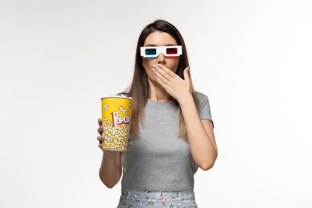 Vooraanzicht jonge vrouw popcorn pakket eten en kijken naar film in d zonnebril op wit bureau