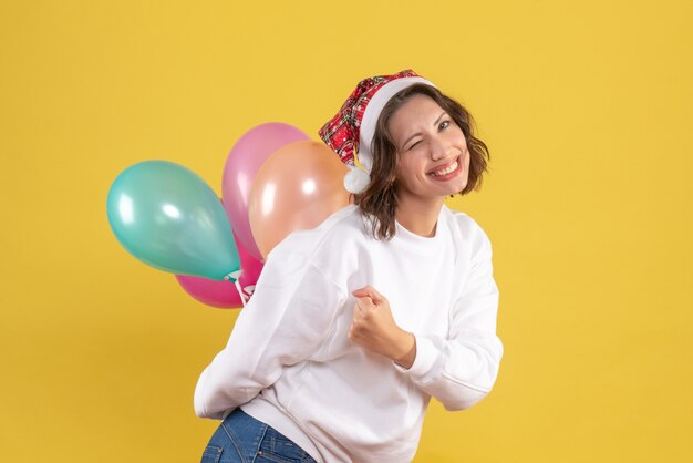 Vooraanzicht jonge vrouw verbergt kleurrijke ballonnen op gele Nieuwjaar kerst kleur vakantie vrouw emotie